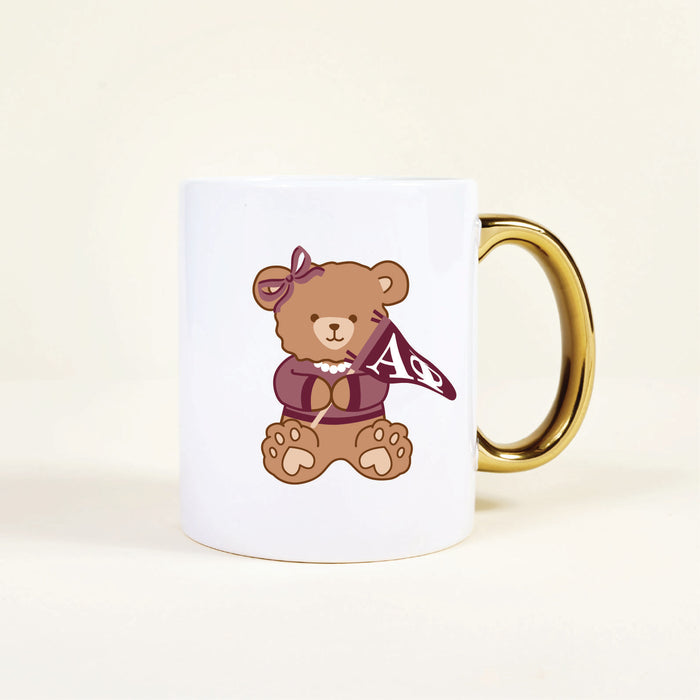 The Darling Effectโs Alpha Phi 11 oz Cozy Cute Ceramic Mug features a teddy bear with a bow and pearl necklace, holding a maroon Aฮฆ flagโa delightful sorority mug to brighten your morning coffee.