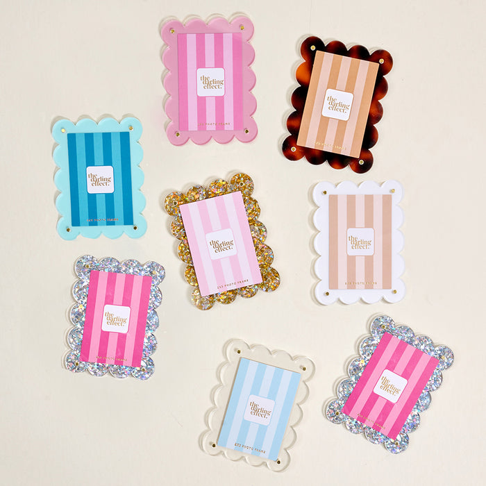 Eight scallop-edged trays in assorted colors and patterns, each labeled "The Collective Effect," are displayed on a light surfaceβperfect for showcasing Blue Mini Acrylic Picture Frame Magnets from The Darling Effect or creating a playful polaroid display.