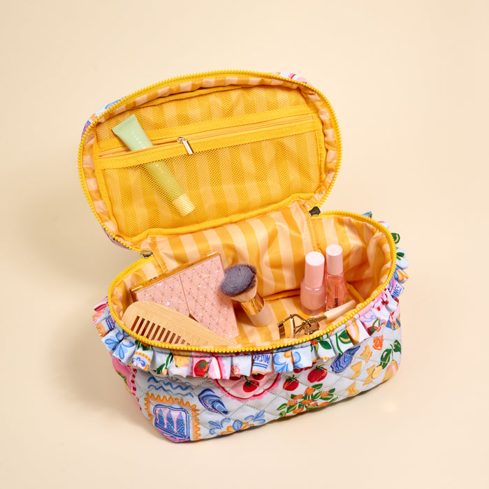 The Darling Effect's Ciao Bella Glam & Go Quilted Cosmetic Bag, featuring a floral pattern and yellow striped interior, is open to reveal cosmeticsβa brush, comb, tubes, compact, and a small green tube in the mesh pocket.