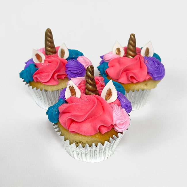 Three Fancy Unicorn Cupcakes with pink, blue, and purple hair, white and gold ears, and golden horns