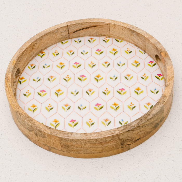 The-darling-effectโs Handpicked For You Large Round Wood Enamel Tray features short sides, cut-out handles, and a white base with a hexagonal colorful floral pattern, displayed on a white speckled surface.