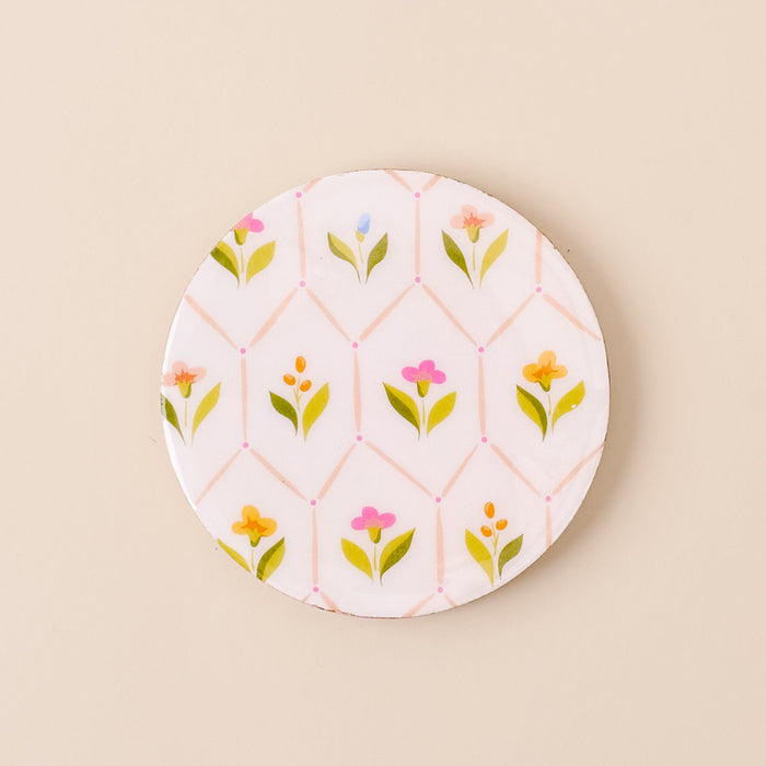 A round ceramic plate with a white background and pastel floral pattern is paired beautifully with the-darling-effect's Handpicked for You Wood Enamel Coaster on a beige surface.