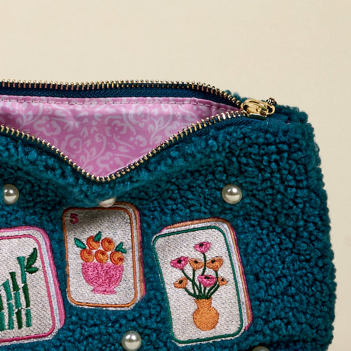 A close-up of The Darling Effectโs "It's Mahj Time Teddy Pouch" in textured teal with a gold zipper, featuring embroidered bamboo, oranges, flowers, decorative pearls, and a pink patterned liningโperfect for your accessory set.