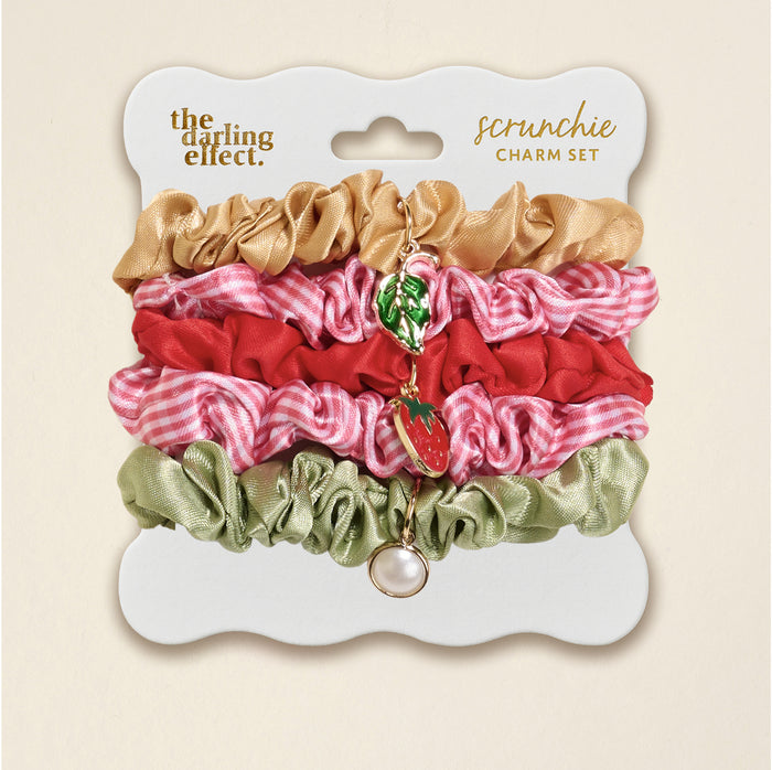 The Darling Effectβs Strawberry Squeeze Scrunchie Charm Set features four stylish hair accessoriesβgold, red, pink gingham, and sage greenβwith gold strawberry, leaf, and pearl charms on a white card labeled βscrunchie set.β.