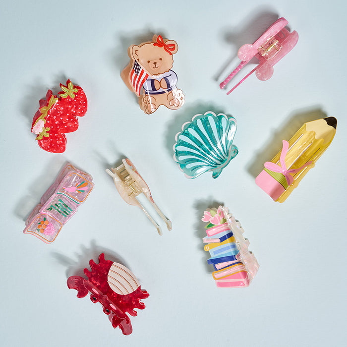 The Darling Effectโs Tomatoes Shape Up Claw Clip, along with other playful designs, sits in a circle on a light blue backgroundโcolorful accessories perfect for adding a cute touch to your hairstyle.