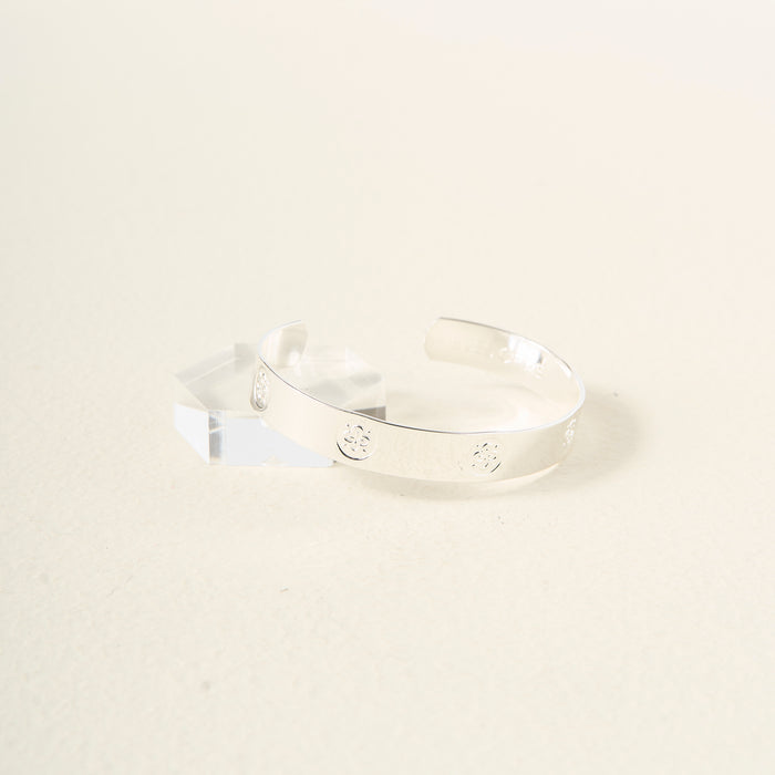 The Darling Effectβs You Are Friendly Trait Cuff Bracelet, crafted in sterling silver with small circular engravings, is shown on a light surface beside a clear geometric acrylic blockβan ideal gift for any occasion.