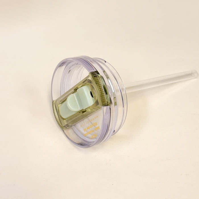 The Darling Effect’s 20 oz Green Lifestyle Flip Straw Replacement Lid features a clear plastic design with a sliding white closure, leak-resistant seal, and attached transparent straw, shown against a plain white background.