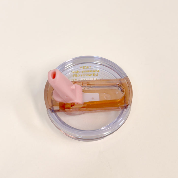 The Darling Effect 20 oz Peach Lifestyle Flip Straw Replacement Lid features a transparent circular design, a brown flip-top, pink silicone straw, and gold-printed text, shown on a plain white surface.