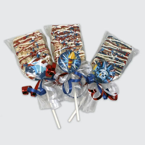 Three Rice Krispy treat pops decorated with red, white, and blue drizzle and patriotic sprinkles, each wrapped in cello with red, white, and blue curling ribbons and topped with themed chocolate medallions; American Eagle, Firecracker, and Statue of Liberty.