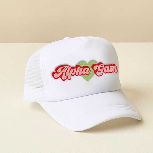 The Darling Effect’s Alpha Gamma Delta White Trucker Hat features a white mesh back and “Alpha Gam” in red script, separated by a green heart—ideal for showing chapter pride. Displayed on beige, with a light beige background.