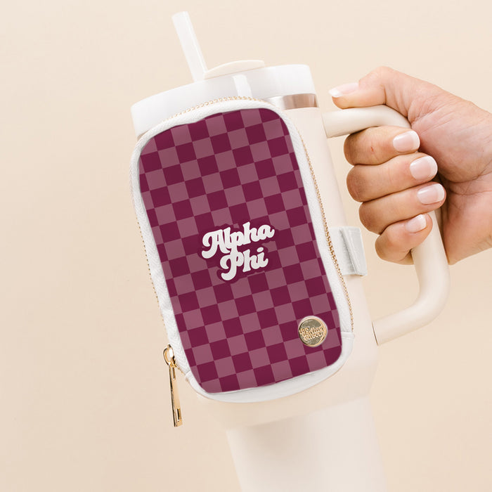 A hand holds a large white tumbler with The Darling Effect’s Alpha Phi Tumbler Fanny Pack, featuring a maroon and pink checkered pattern and “Alpha Phi” in white script, attached to the handle.