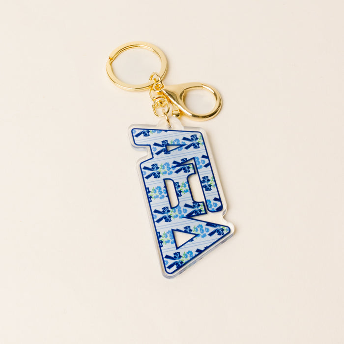 The Darling Effect Alpha Xi Delta Oh So Fancy Letter Acrylic Keychain features a gold keyring and a blue-and-white floral “B” charm—a stylish accessory and perfect sisterhood gift.