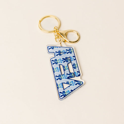 The Darling Effect Alpha Xi Delta Oh So Fancy Letter Acrylic Keychain features a gold keyring and a blue-and-white floral “B” charm—a stylish accessory and perfect sisterhood gift.