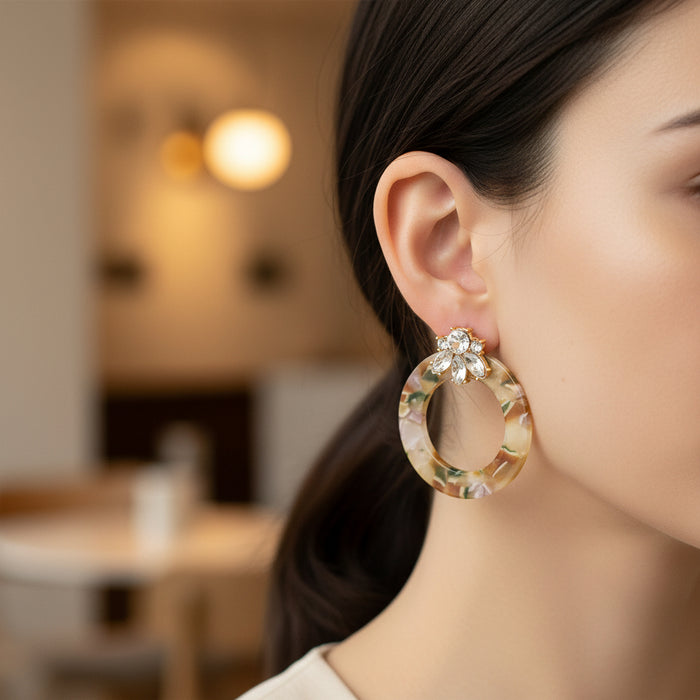 A close-up of a woman's ear wearing The Darling Effect Amber Drift Glow Getter Earrings—lightweight, marbled acetate hoops accented with sparkling, clear stones.