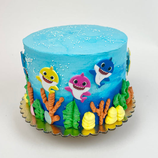 A decorated cake with Baby Shark characters and sea life accents in blue, pink, yellow, and green colors.