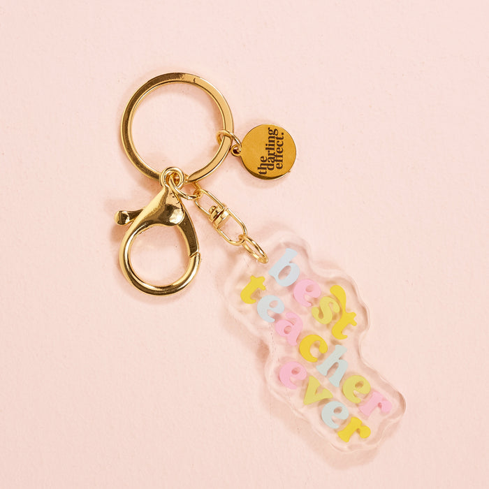 The Best Teacher Ever Acrylic Keychain by the-darling-effect is a pocket-sized gold keychain with a lobster clasp, a "The Learning Club" charm, and a pastel acrylic tag reading "best teacher ever" on pink—a cute accessory for any collection.