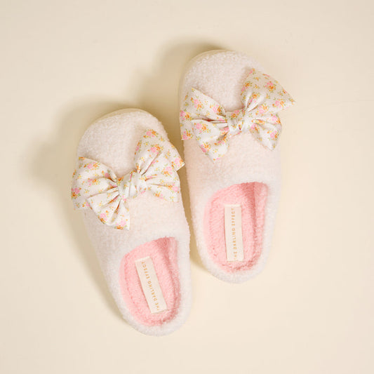 The Darling Effect's Betty Bow Endless Daydream Cream Fuzzy Slippers feature floral bows and pink soles, offering cozy comfort and stylish flair for relaxing at home.