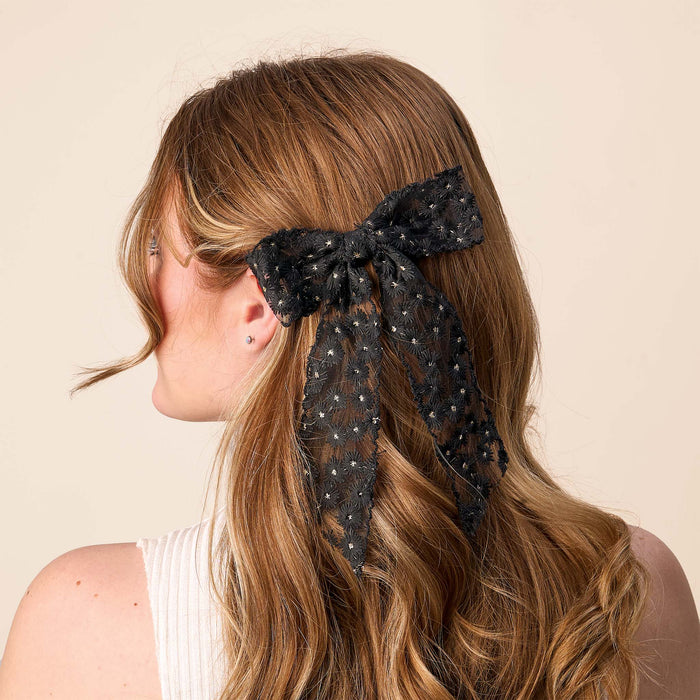 A woman's back is shown with wavy auburn hair pulled back by the-darling-effect's Black Ditzy Daisies Hair Bow, featuring delicate floral details and a gold barrette clip for an elegant finish.