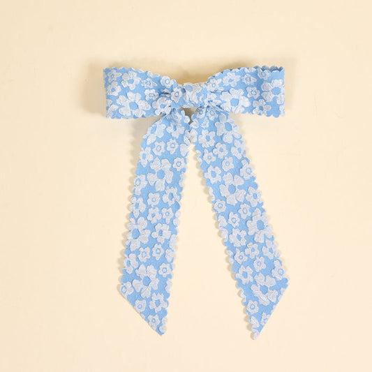 The Blue Flower Scallop Hair Bow by the-darling-effect features white floral embroidery and scalloped edges—a charming addition to your hair accessories. Shown on a pale yellow background.