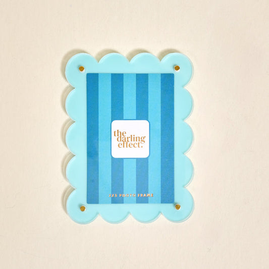 The Darling Effect Blue Mini Acrylic Picture Frame Magnet features scalloped edges, vertical blue stripes, and a white brand label. It perfectly fits 2x3 Polaroids and is ideal for displaying your favorite photos on the fridge.
