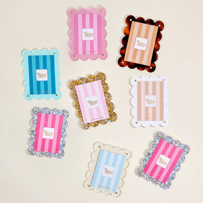 Eight scallop-edged trays in assorted colors and patterns, each labeled "The Collective Effect," are displayed on a light surface—perfect for showcasing Blue Mini Acrylic Picture Frame Magnets from The Darling Effect or creating a playful polaroid display.