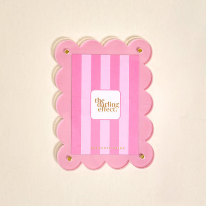 The Darling Effect’s Blush Mini Acrylic Picture Frame Magnet features scalloped edges, vertical blush stripes, and four gold corner bolts—perfect for displaying polaroid photos. The center displays a card with the brand name.