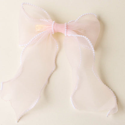 The-darling-effect's Blush Sheer Pearl Hair Bow features sheer pink fabric, a satin center, and a pearl-trimmed border—an elegant addition to your hair accessories collection.