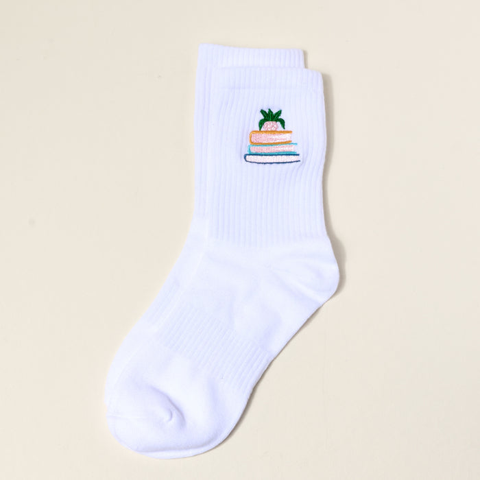 The Book Nook Embroidered Crew Sock is a single white women’s sock with a pineapple perched on three books design—ideal for those who love unique, colorful socks.