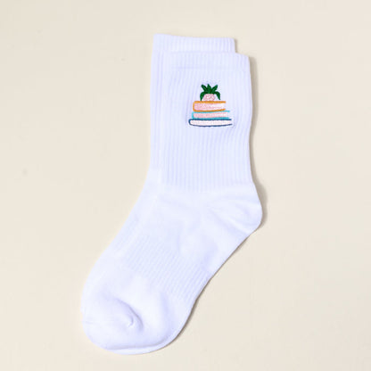 The Book Nook Embroidered Crew Sock is a single white women’s sock with a pineapple perched on three books design—ideal for those who love unique, colorful socks.