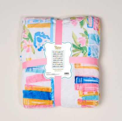 The Darling Effect Book Shelfie Snuggle Up Plush Blanket is a folded, cozy throw with colorful floral and geometric patterns, wrapped in a pink ribbon and decorative label, displayed on a light background.