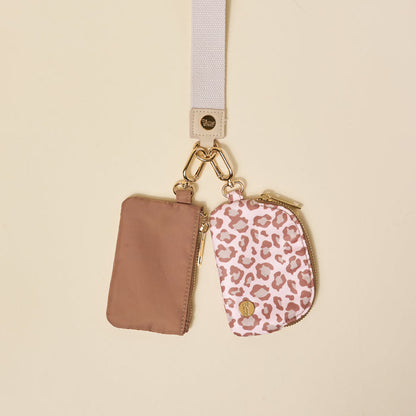 The Darling Effect’s Born Wild Dynamic Duo Pouch Wristlet features two small zippered pouches—one beige, one pink leopard print—attached to a white lanyard with gold hardware, shown against a light beige background.