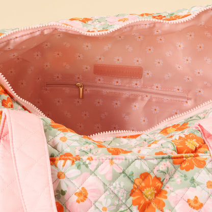 The-darling-effect’s Bouquet Beauty Sage On-the-Go Quilted Weekender Bag features pink handles, an orange, pink, and green floral pattern, a light pink daisy-print interior with a zip pocket—combining style and spacious travel convenience.