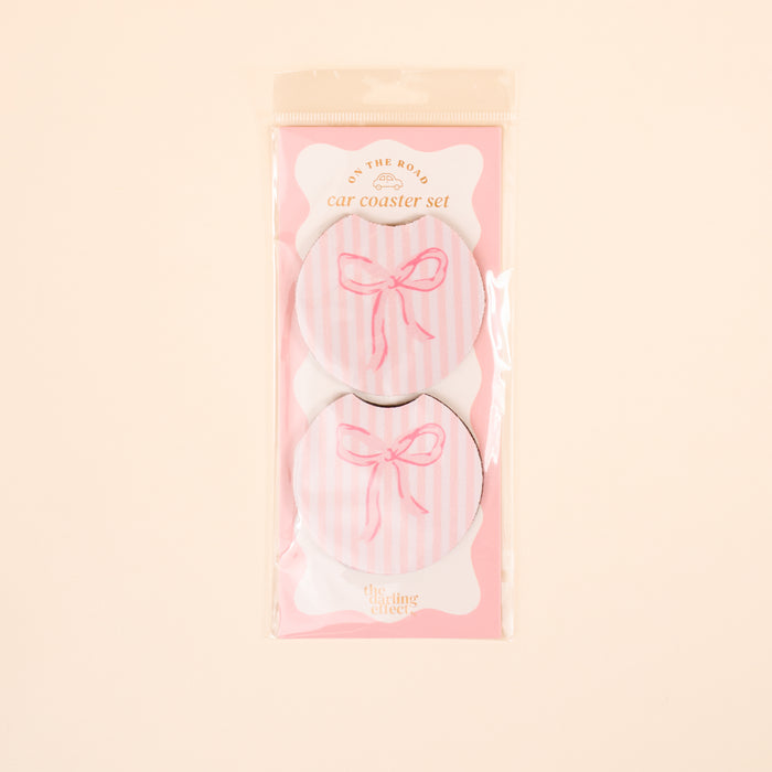 The Darling Effect Bow Pink On the Road Car Coaster Set includes two round, absorbent car coasters with pink and white stripes, each featuring a pink bow design on a light beige background.