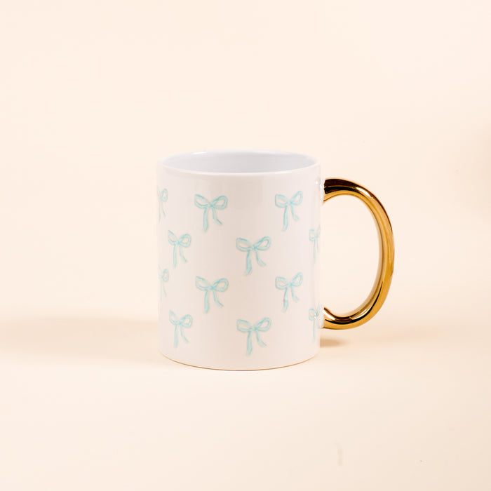 The Darling Effect’s Bows Blue 11 oz Cozy Cute Ceramic Mug features a golden handle and charming light blue bow pattern—perfect for enjoying coffee or tea.