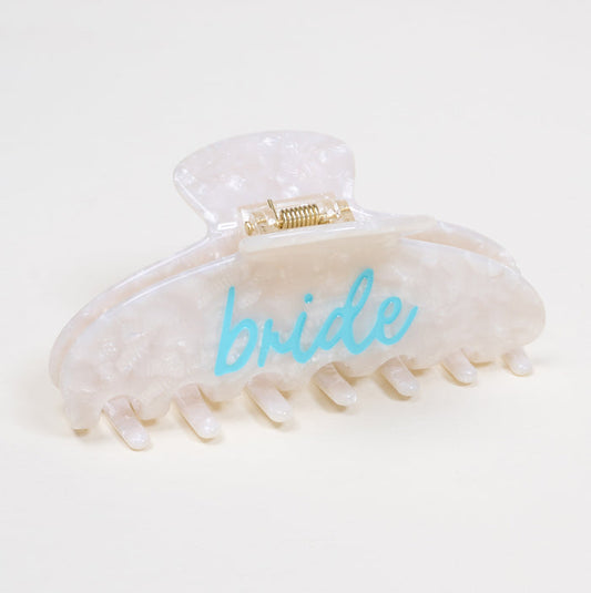 The Darling Effect’s Bridal Word Up Claw Clip features a white marbled design with “bride” in light blue script, perfect for a playful hairstyle accent. Shown on a plain light background.