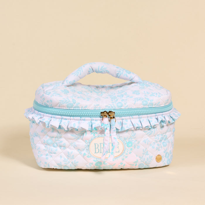 The Darling Effect Bride Something Blue Glam & Go Quilted Cosmetic Bag features pastel blue and white florals, a handle, ruffled trim, dual zippers, and an oval BRIDE patch—a charming accessory for any bride on the go.