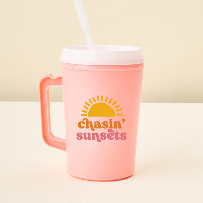 The-darling-effect’s Chasin' Sunsets 34oz Mega Mug is a large pink plastic tumbler with handle, white lid, straw, sun graphic, and "chasin sunsets" in yellow and pink—perfect event drinkware for any occasion.
