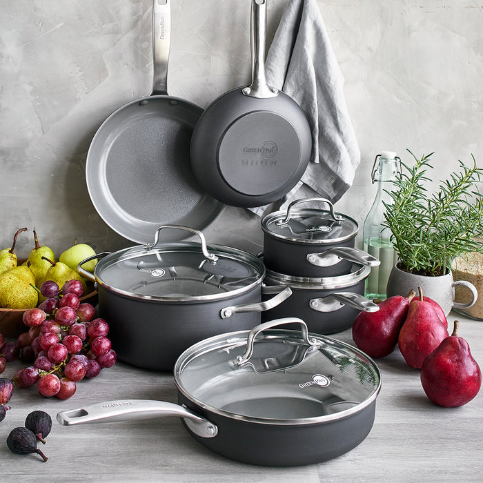 Ten-piece ceramic nonstick cookware set with lids on a countertop, fruits and herbs arranged nearby.