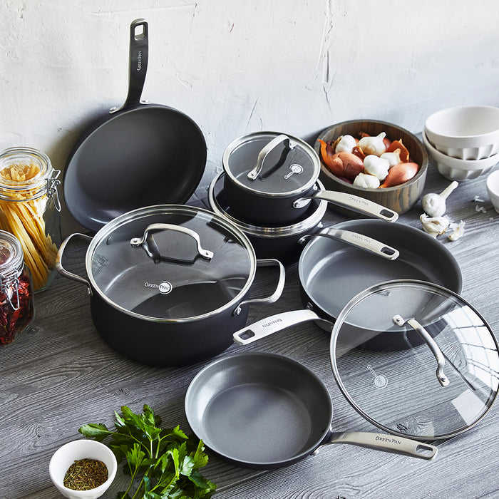 Gray ceramic nonstick 10-piece cookware set with glass lids on a kitchen counter, surrounded by herbs, pasta, and vegetables.
