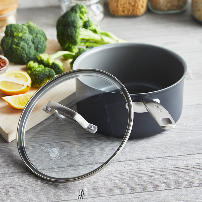 Gray ceramic nonstick saucepan with lid on wood counter, next to broccoli, lemons, and assorted vegetables.