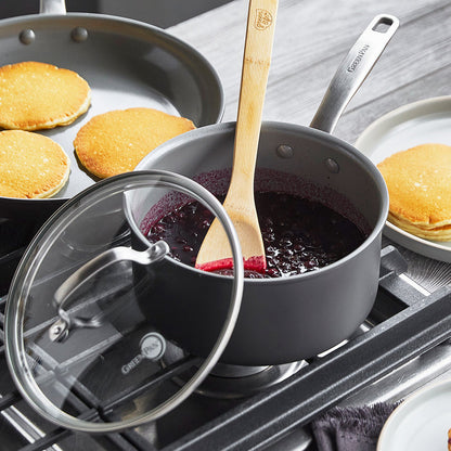 Blueberry sauce in a ceramic nonstick saucepan next to pancakes cooking in a skillet on a stove.