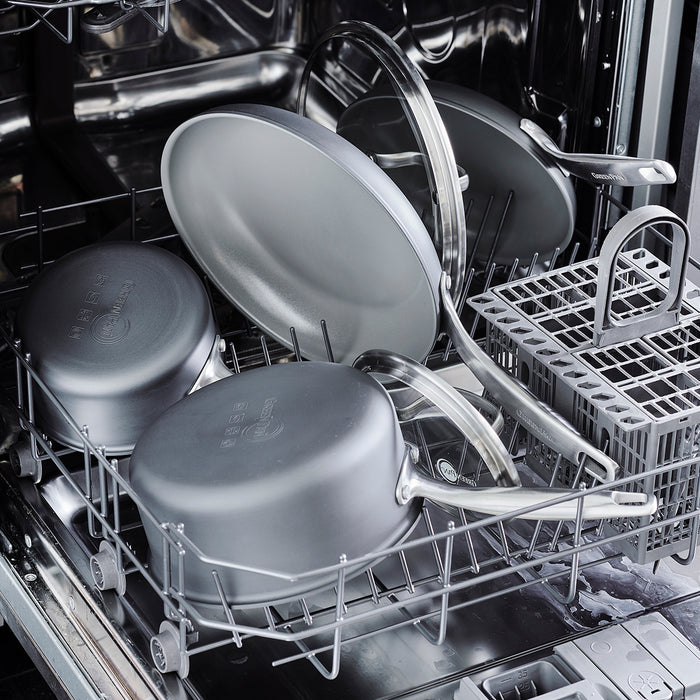 Ceramic nonstick saucepan with lid in silver color placed on the bottom rack of an open dishwasher.