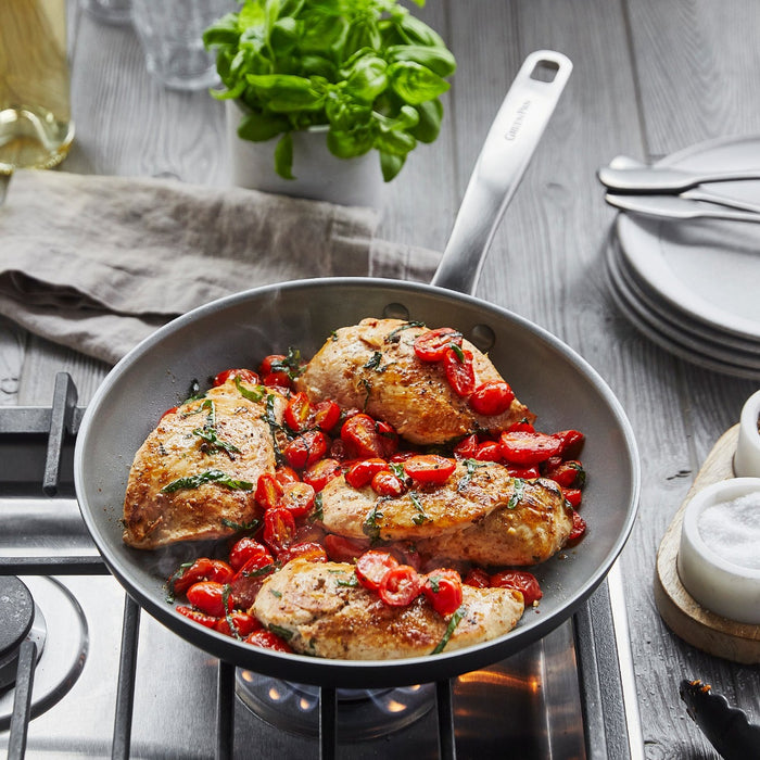 Tomato and herb chicken cooking in a ceramic nonstick frypan set, with plates and fresh basil nearby.