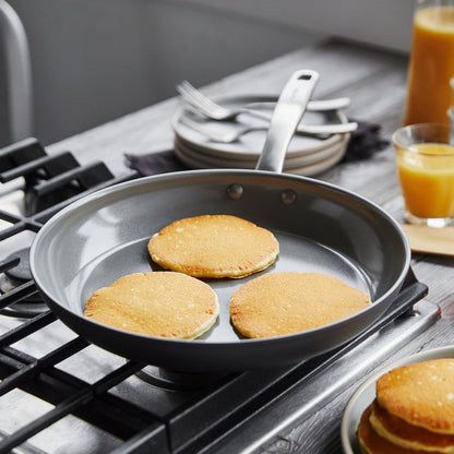 Pancakes cooking in a Chatham ceramic nonstick 8-inch frypan, with plates and orange juice in the background.