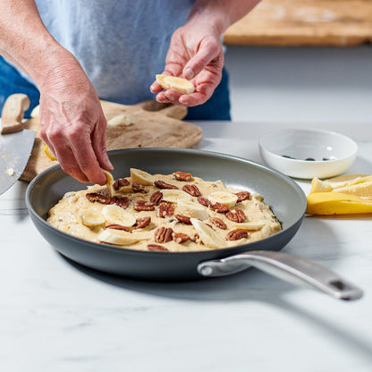 Sliced bananas and pecans being added to batter in an 8-inch Chatham Ceramic Nonstick frypan on a white counter.