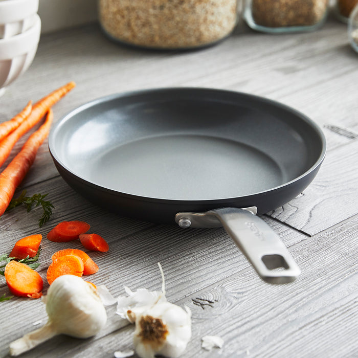 Gray ceramic nonstick 8-inch frypan with metal handle on counter next to carrots and garlic.