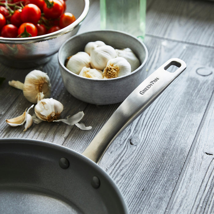 Ceramic nonstick 8-inch frypan with garlic bulbs and cherry tomatoes on a wooden table in a metal strainer.