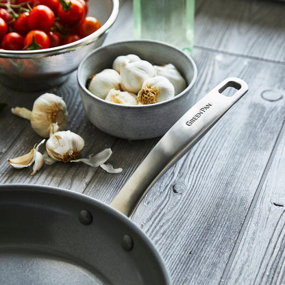 Ceramic nonstick 8-inch frypan with garlic bulbs and cherry tomatoes on a wooden table in a metal strainer.