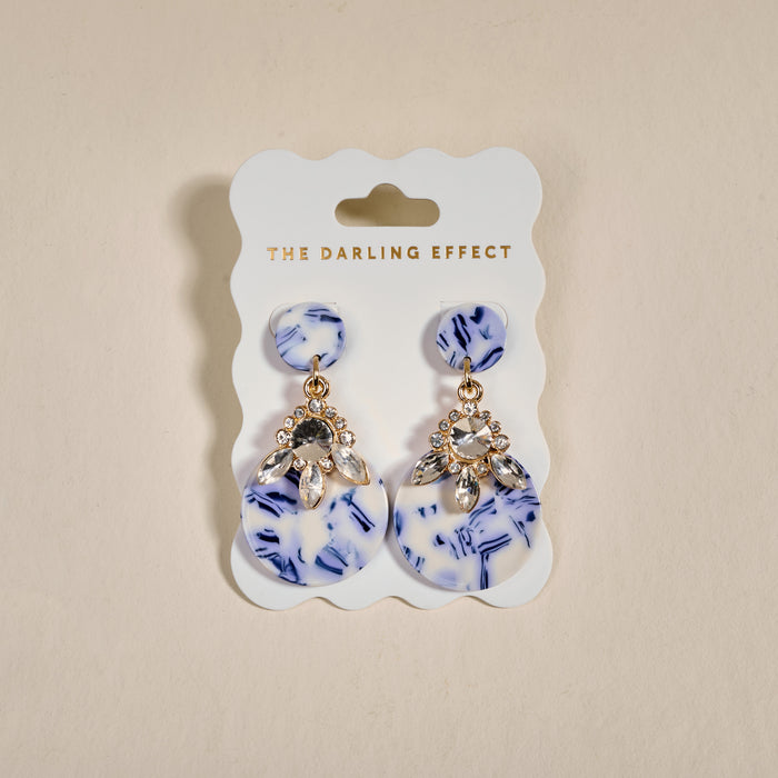 The Darling Effect’s Chinoiserie Flair Show Stopper Earrings feature blue and white marbled discs with clear rhinestones. Lightweight and modern, they add a unique, contemporary touch to any outfit.