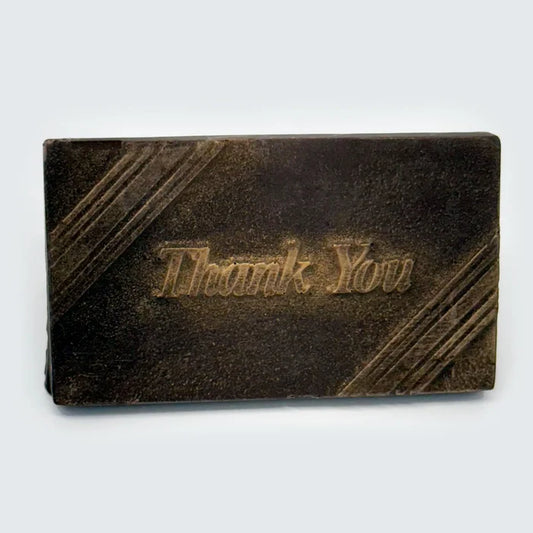 An elegant rectangular chocolate favor features rich brown finish accented with a delicate touch of gold dust for a luxurious shimmer. Subtle diagonal lines frame the design, while the words “Thank You” are gracefully embossed in the center.